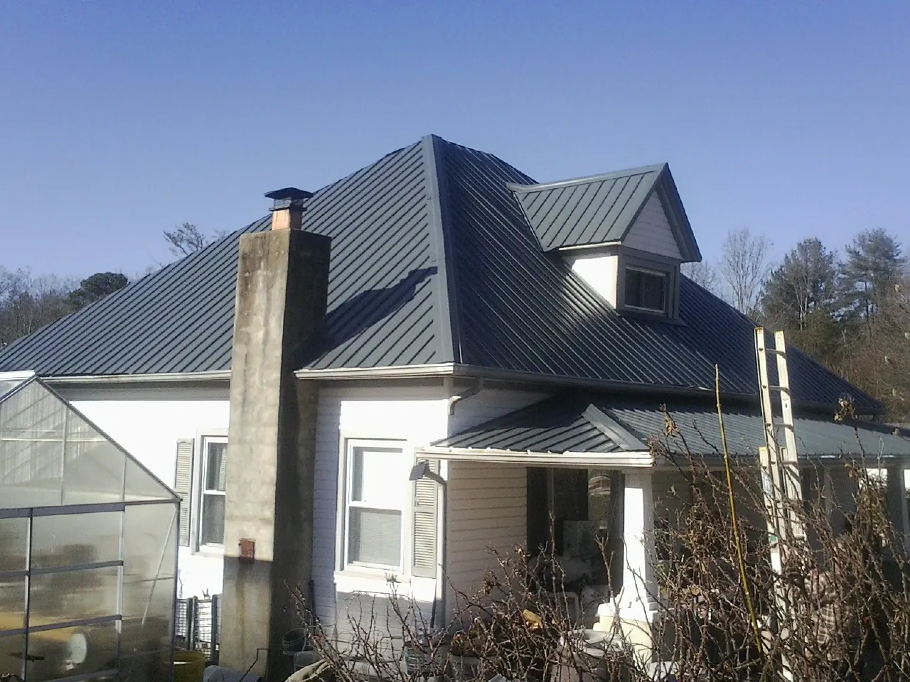 Dark blue standing seam metal roof on a white farmhouse with dormer — Slate & Tile Roof Repair by Roofing Brothers in Riverhead