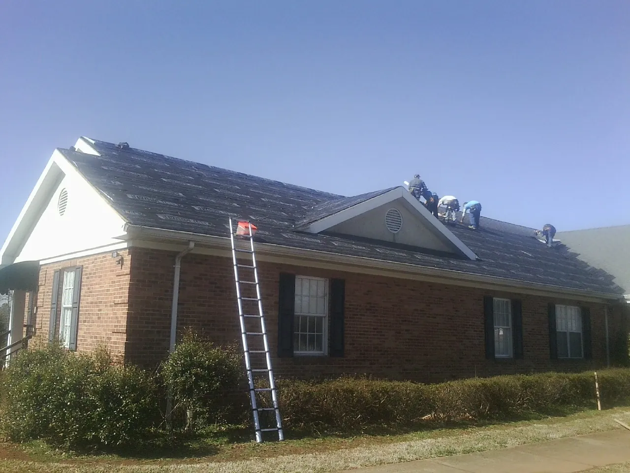 Crew tearing shingles off a brick ranch roof with a ladder set — Emergency Roof Repair work by our crew in Riverhead