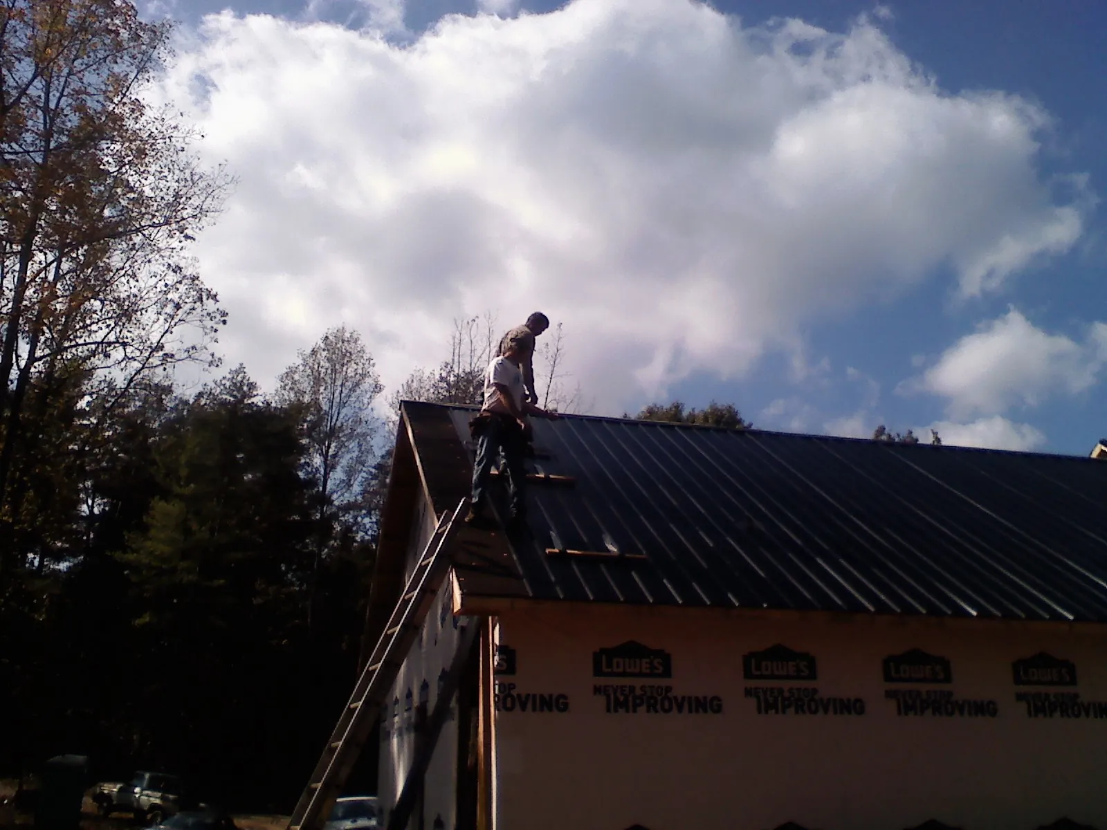 Roofer fastening dark metal panels high against a cloudy sky, from a Roof Inspection job in Riverhead