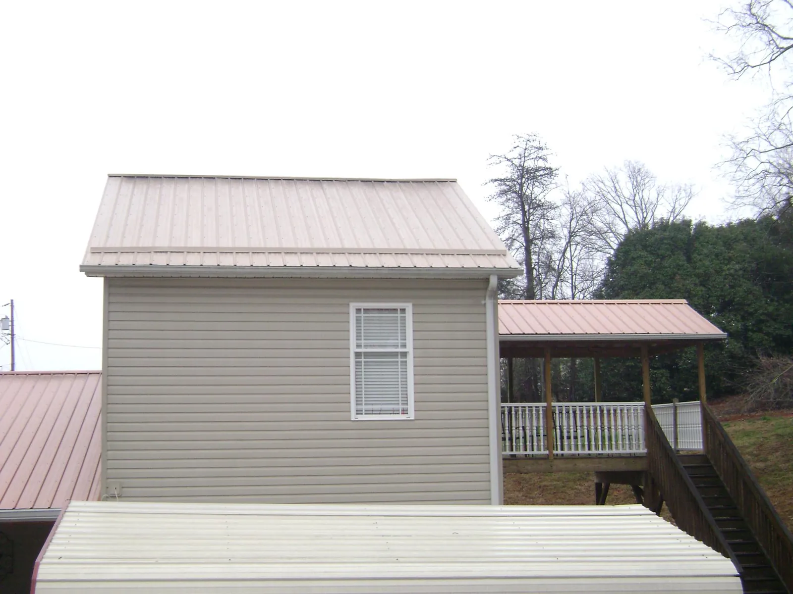 Tan metal roofs on a two story addition and attached porch, from a Roof Replacement job in Riverhead